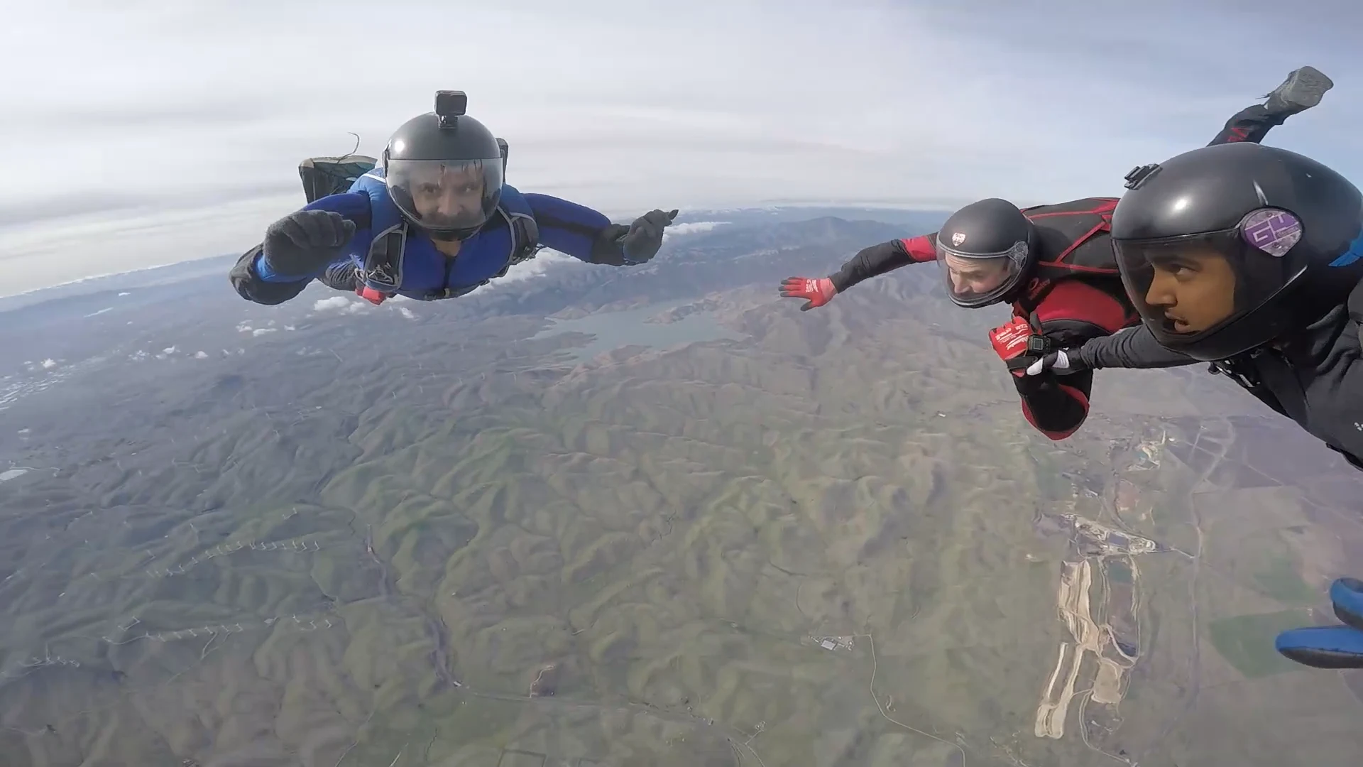 Umar Rafi in a blue suit skydiving alongside two fellow skydivers above a mountainous landscape