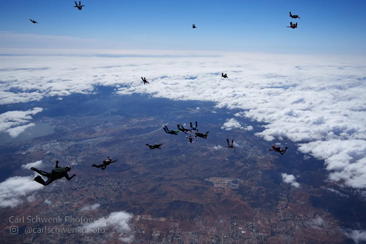 Skydivers descending over a broad landscape and clouds