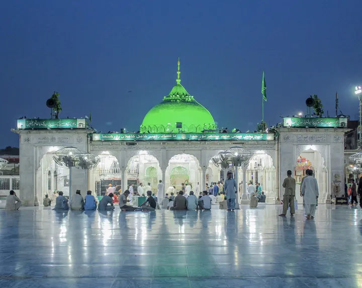 The green-domed shrine of Data Darbar in Lahore at dusk, with pilgrims in the marble courtyard