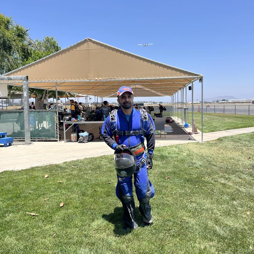 Umar Rafi in his blue skydiving suit, holding his helmet on the ground